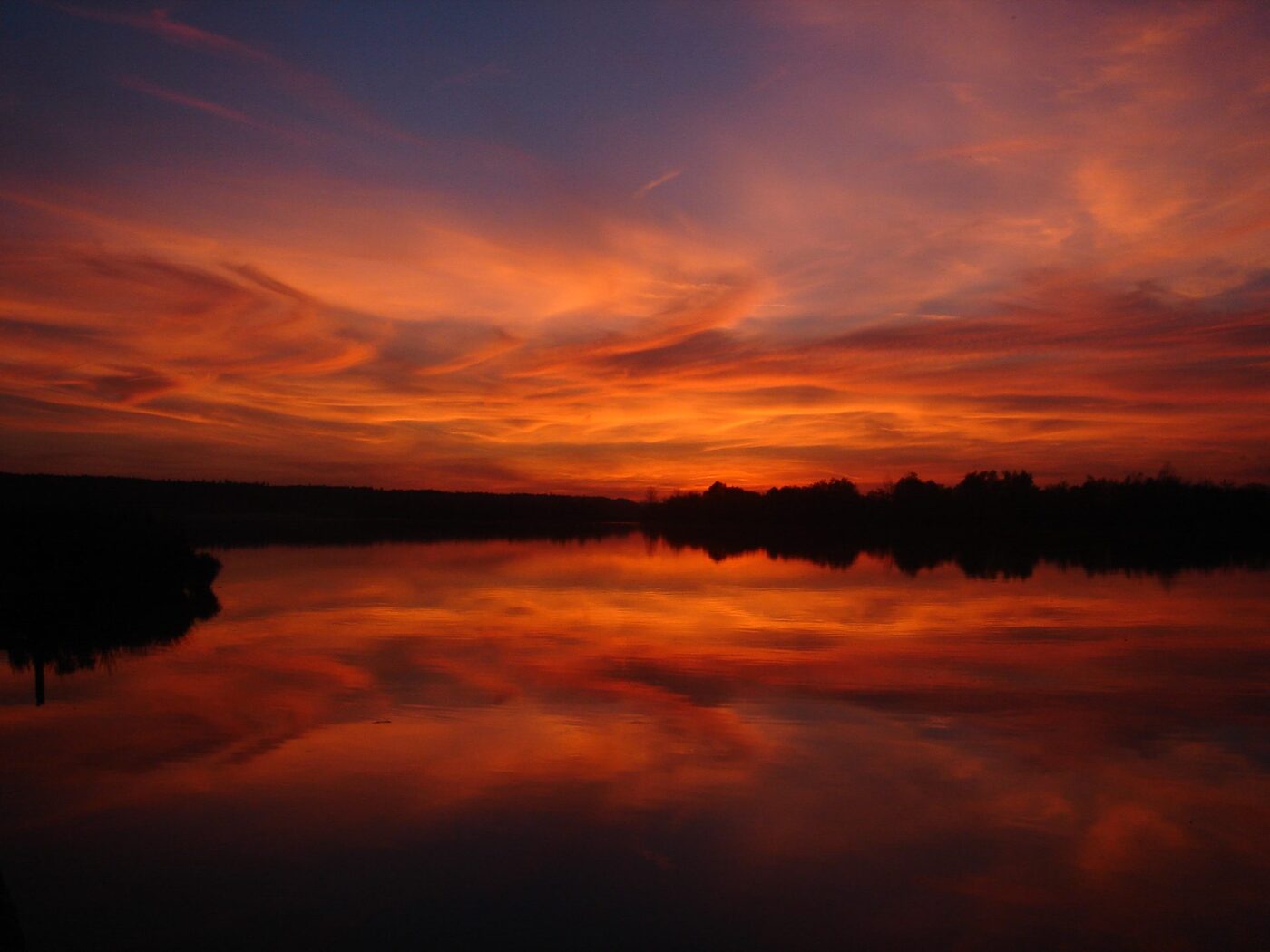 Austrian lake at sunset — crimson reflection on still water, echoing Daniel Harner's European roots