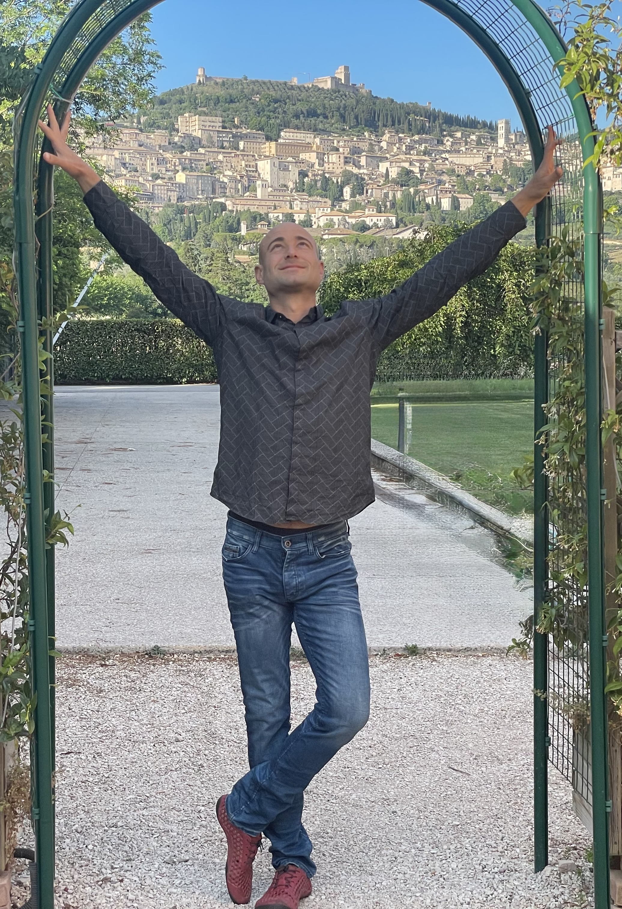 Daniel Harner standing in a garden archway with the hilltop town of Assisi behind him